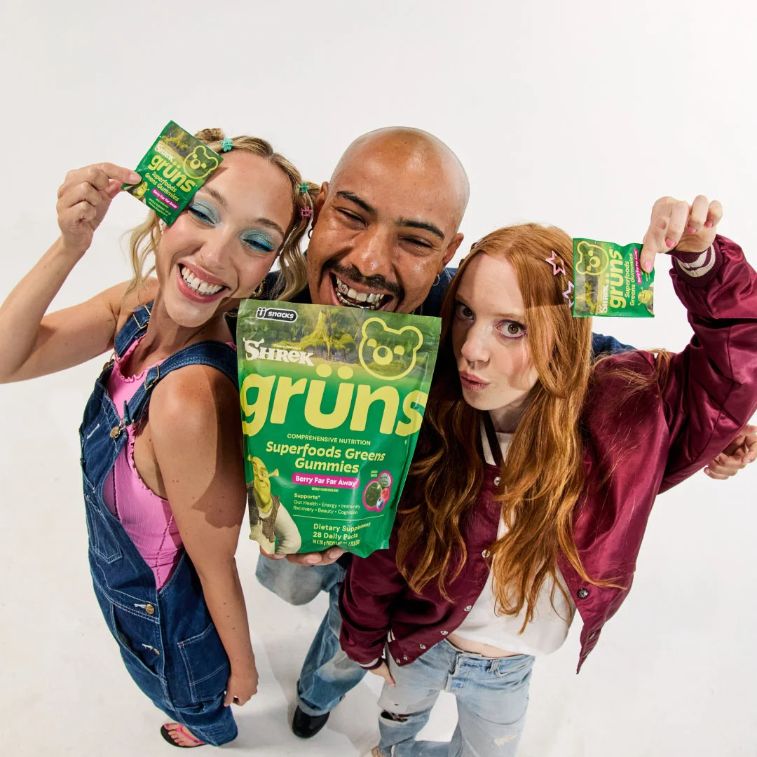 Three people posing playfully, each holding up a green Shrek Grüns pouch